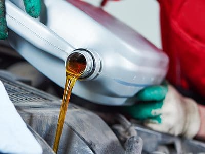 Person pouring a gallon of oil into a car engine