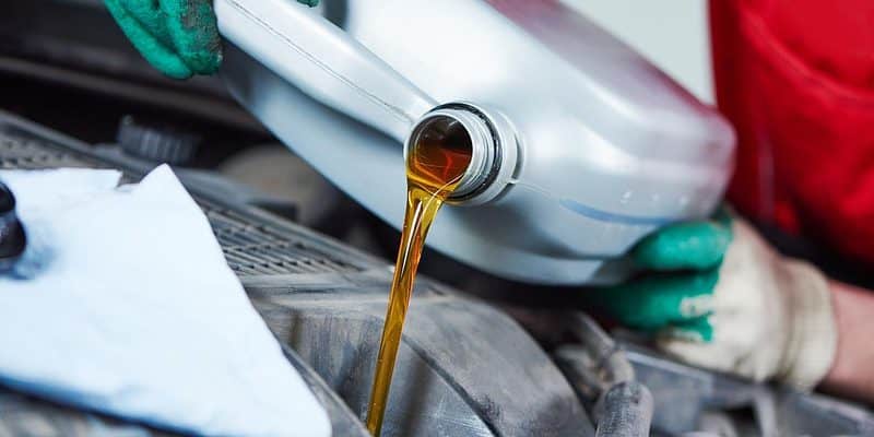 Person pouring a gallon of oil into a car engine