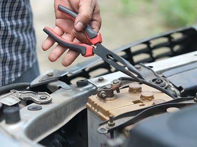 Person holding pliers to a car battery