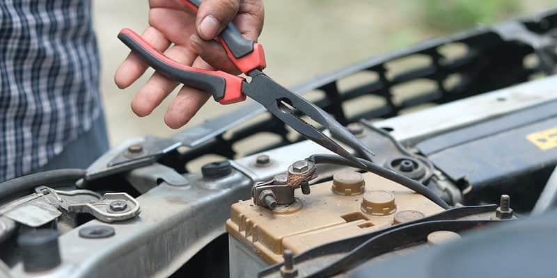 Person holding pliers to a car battery