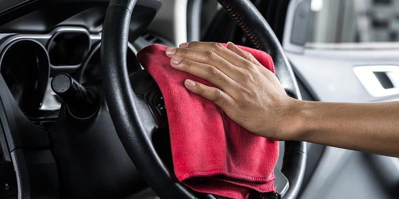 using a red towel to clean a car steering wheel