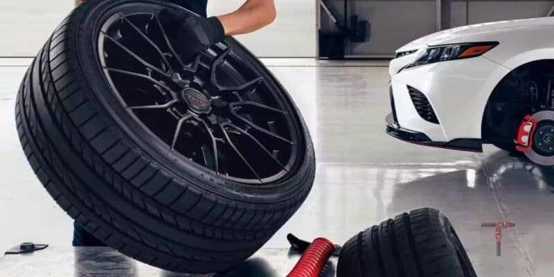 Technician holding a car tire with a white Camry in the background